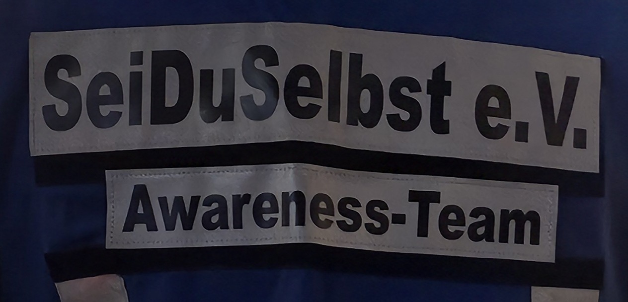 Rückenschild mit der Aufschrift „SeiDuSelbst e.V. – Awareness-Team“, getragen von einem Teammitglied beim Pink Monday auf dem Düsseldorfer Weihnachtsmarkt 2025.